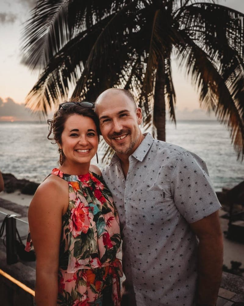 Justin Cateron smiling at sunset by the ocean, under a palm tree